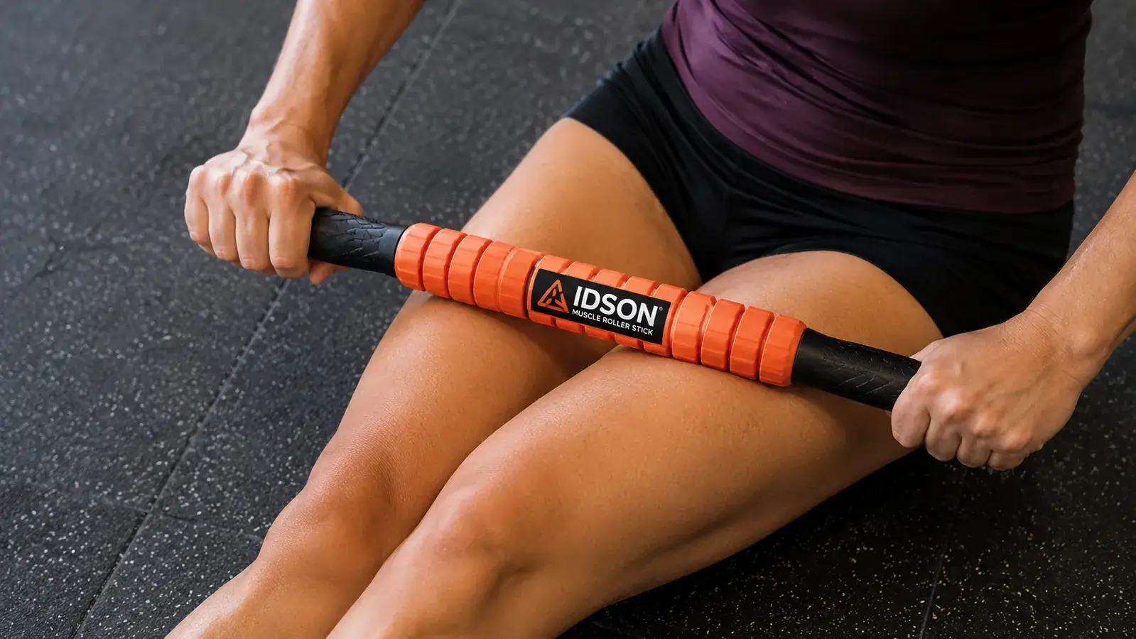 Close-up of hands pressing an Idson roller stick into a quadricep muscle on the front of the thigh
