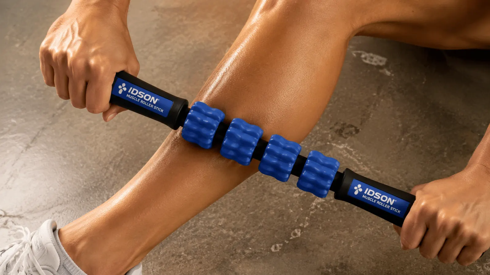 Close-up of hands gripping a muscle roller stick against a bare calf muscle
