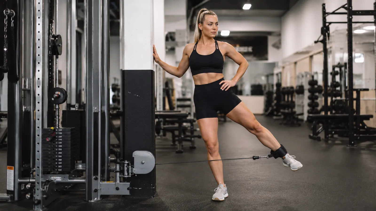 Athlete using a cable machine for a standing hip abduction stretch in a commercial gym